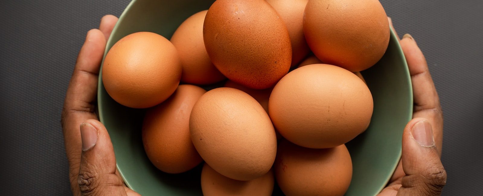 person holding brown egg on green ceramic bowl