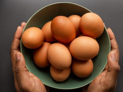 person holding brown egg on green ceramic bowl