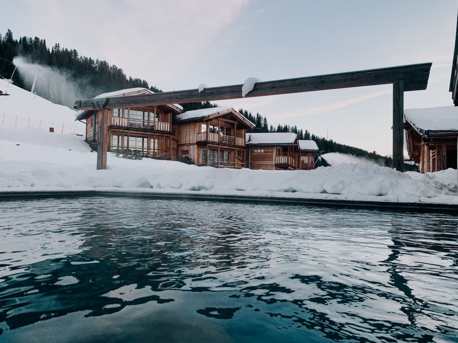 Where Can I Find a Large Alpine Spa Hotel in Tyrol? Idyllic wooden cabins by a lake in a snowy Italian village, showcasing winter beauty