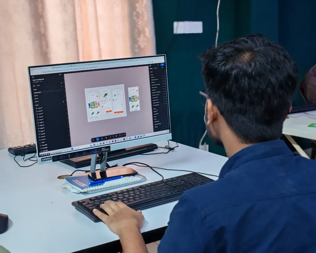 A young designer focused on creating user interfaces on a desktop computer in an office setting